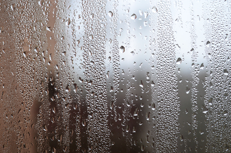 A photo of the glass surface of the window, covered with a multitude of droplets of various sizes. Background texture of a dense layer of condensate on glassの写真素材