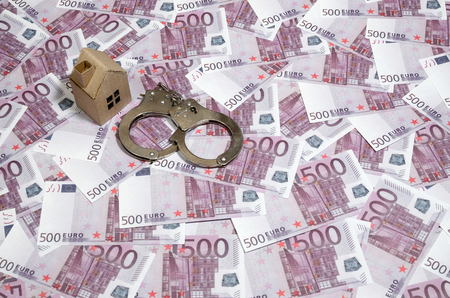 Scam with real estate. Cheating when buying or renting a house. Punishment for deception. A toy house with handcuffs on a many 500 purple euro banknotesの写真素材