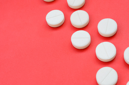 A few white tablets lie on a bright red background surface. Background image on medical and pharmaceutical topicsの写真素材