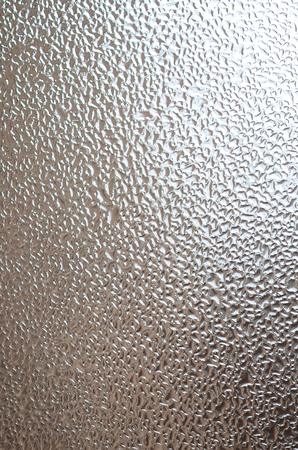 A photo of the glass surface of the window, covered with a multitude of droplets of various sizes. Background texture of a dense layer of condensate on glassの写真素材