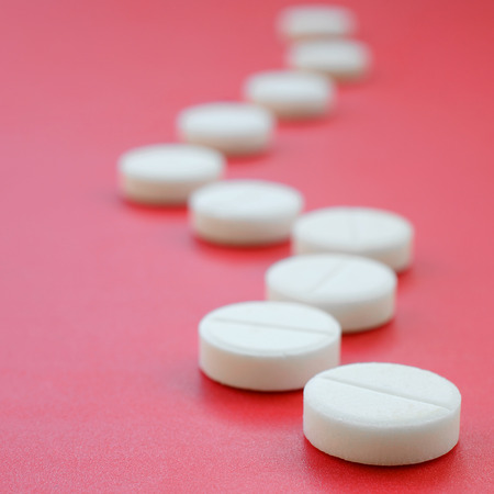 A few white tablets lie on a bright red background surface. Background image on medical and pharmaceutical topicsの写真素材