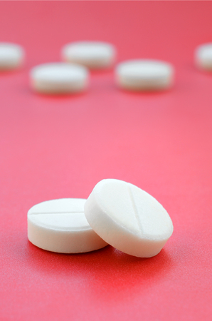 A few white tablets lie on a bright red background surface. Background image on medical and pharmaceutical topicsの写真素材