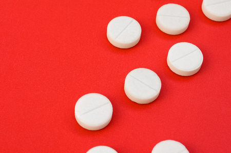 A few white tablets lie on a bright red background surface. Background image on medical and pharmaceutical topicsの写真素材