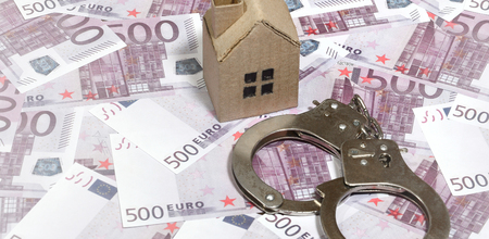 Scam with real estate. Cheating when buying or renting a house. Punishment for deception. A toy house with handcuffs on a many 500 purple euro banknotesの写真素材