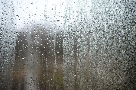 A photo of the glass surface of the window, covered with a multitude of droplets of various sizes. Background texture of a dense layer of condensate on glassの写真素材
