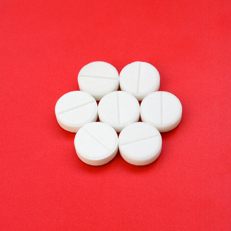 A few white tablets lie on a bright red background surface. Background image on medical and pharmaceutical topicsの写真素材