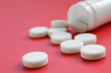Several white tablets fall out of the plastic jar on the red surface. Background image on medical and pharmaceutical topicsの写真素材
