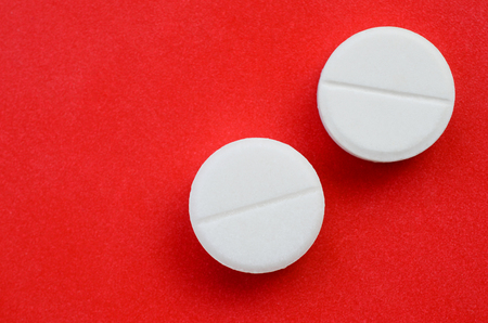 A few white tablets lie on a bright red background surface. Background image on medical and pharmaceutical topicsの写真素材