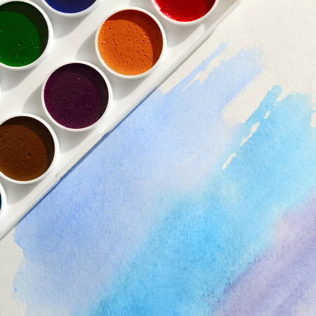 A new set of watercolors lies on a sheet of paper, which shows an abstract watercolor drawing in the form of blue strokes. The concept of amateur painting among teenagersの写真素材