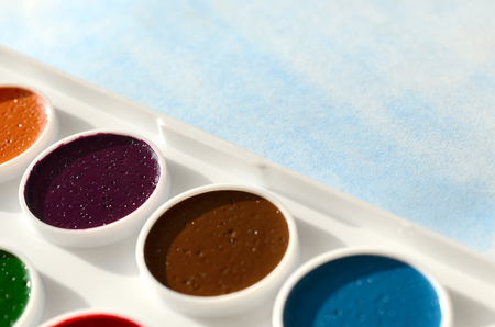 A new set of watercolors lies on a sheet of paper, which shows an abstract watercolor drawing in the form of blue strokes. The concept of amateur painting among teenagersの写真素材