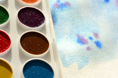A new set of watercolors lies on a sheet of paper, which shows an abstract watercolor drawing in the form of blue strokes. The concept of amateur painting among teenagersの写真素材
