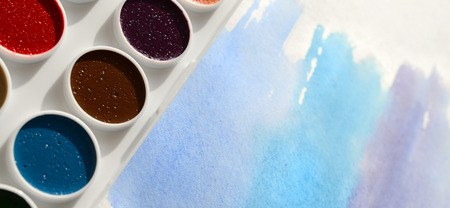 A new set of watercolors lies on a sheet of paper, which shows an abstract watercolor drawing in the form of blue strokes. The concept of amateur painting among teenagersの写真素材