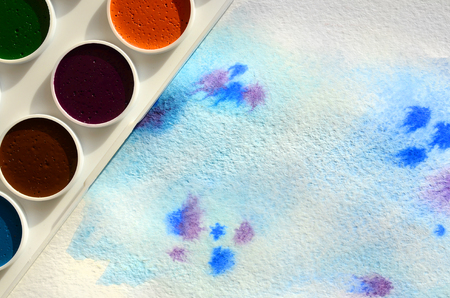 A new set of watercolors lies on a sheet of paper, which shows an abstract watercolor drawing in the form of blue strokes. The concept of amateur painting among teenagersの写真素材