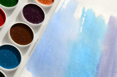 A new set of watercolors lies on a sheet of paper, which shows an abstract watercolor drawing in the form of blue strokes. The concept of amateur painting among teenagersの写真素材
