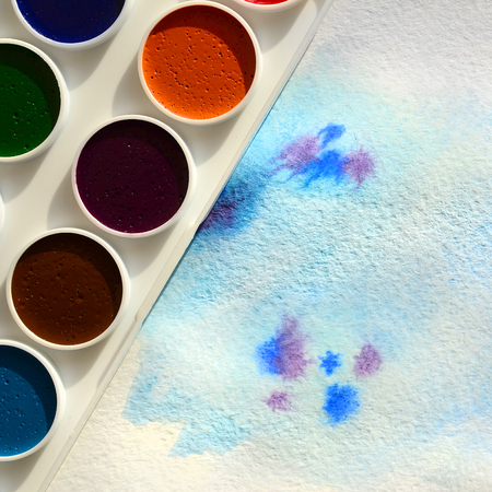 A new set of watercolors lies on a sheet of paper, which shows an abstract watercolor drawing in the form of blue strokes. The concept of amateur painting among teenagersの写真素材