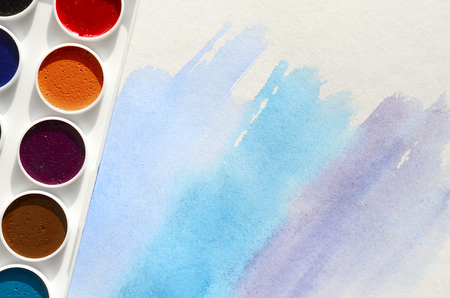 A new set of watercolors lies on a sheet of paper, which shows an abstract watercolor drawing in the form of blue strokes. The concept of amateur painting among teenagersの写真素材