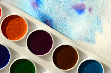 A new set of watercolors lies on a sheet of paper, which shows an abstract watercolor drawing in the form of blue strokes. The concept of amateur painting among teenagersの写真素材
