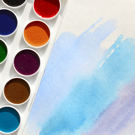 A new set of watercolors lies on a sheet of paper, which shows an abstract watercolor drawing in the form of blue strokes. The concept of amateur painting among teenagersの写真素材