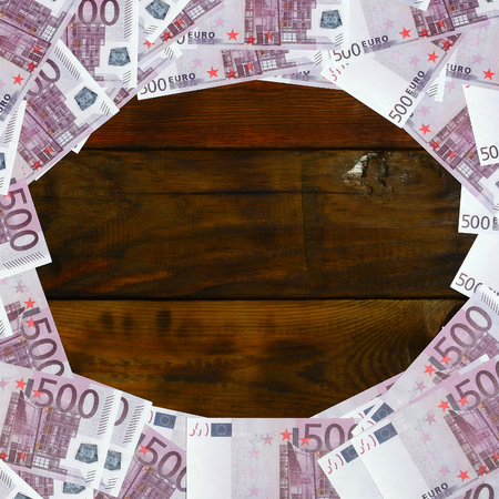 A lot of purple denominations worth 500 euros lie on a wooden surface with an empty pad in the middle of the image. Copy space for textの写真素材