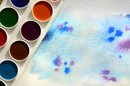 A new set of watercolors lies on a sheet of paper, which shows an abstract watercolor drawing in the form of blue strokes. The concept of amateur painting among teenagersの写真素材