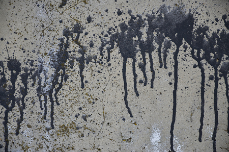 A photograph of a close-up of black paint spots on a concrete wall. Pouring paint on the wall in random order. The concept of graffiti and street art cultureの写真素材