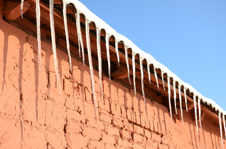 A lot of long icicles hang under the roof of a red brick buildingの写真素材
