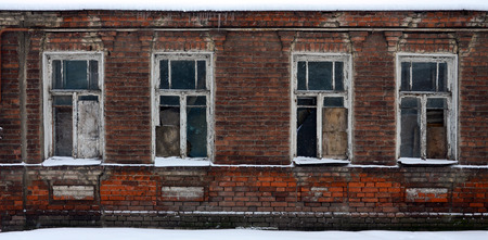 An old brick wall of an apartment house with a lot of boarded up windows without glassの写真素材