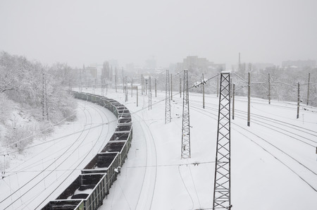 A long train of freight cars is moving along the railroad track. Railway landscape in winter after...