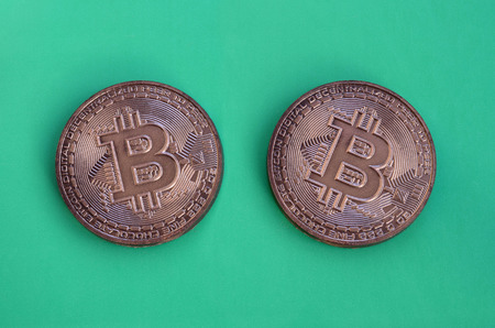 Two chocolate products in the form of physical bitcoins lie on a green plastic background. Model of the crypto currency in the edible formの写真素材