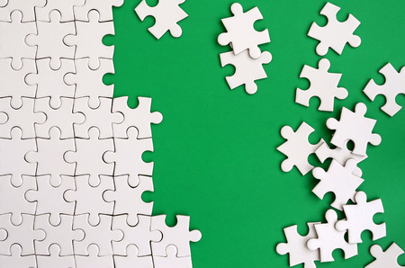 Fragment of a folded white jigsaw puzzle and a pile of uncombed puzzle elements against the background of a green surface. Texture photo with space for textの写真素材
