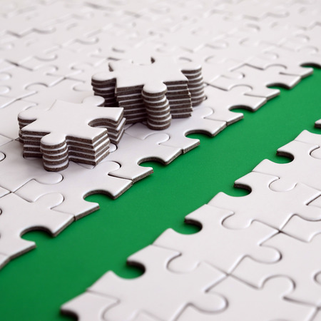 The green path is laid on the platform of a white folded jigsaw puzzle. The missing elements of the puzzle are stacked nearby. Texture image with space for textの写真素材