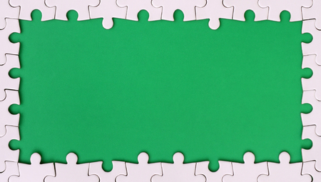 Framing in the form of a rectangle, made of a white jigsaw puzzle around the green spaceの写真素材
