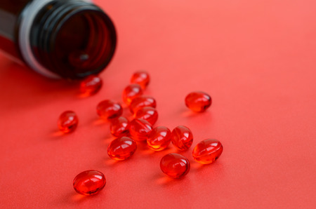 A lot of transparent red tablets were scattered from a small glass brown jar on a red surfaceの写真素材