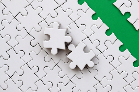 The green path is laid on the platform of a white folded jigsaw puzzle. The missing elements of the puzzle are stacked nearby. Texture image with space for textの写真素材