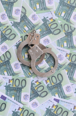 Police handcuffs lies on a set of green monetary denominations of 100 euros. A lot of money forms an infinite heapの写真素材
