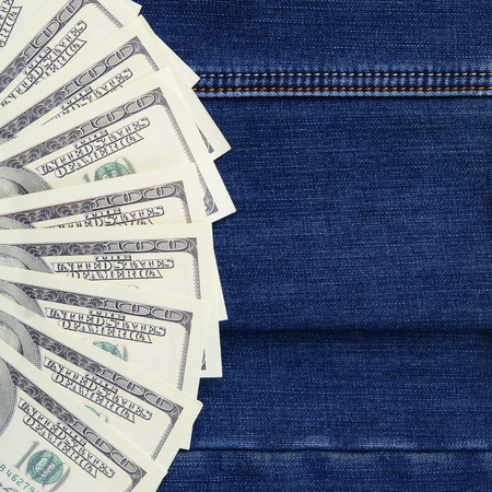 The fan of a lot of US dollars is on a dark denim surface. Background image