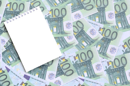 White notebook with clean pages lying on a set of green monetary denominations of 100 euros. A lot of money forms an infinite heapの写真素材