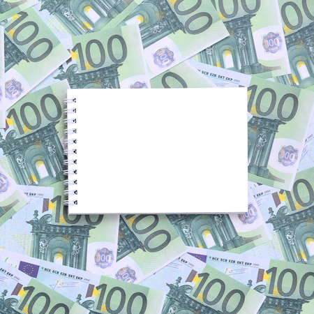 White notebook with clean pages lying on a set of green monetary denominations of 100 euros. A lot of money forms an infinite heapの写真素材
