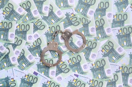 Police handcuffs lies on a set of green monetary denominations of 100 euros. A lot of money forms an infinite heapの写真素材