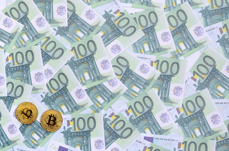 Golden physical bitcoins is lies on a set of green monetary denominations of 100 euros. A lot of money forms an infinite heapの写真素材