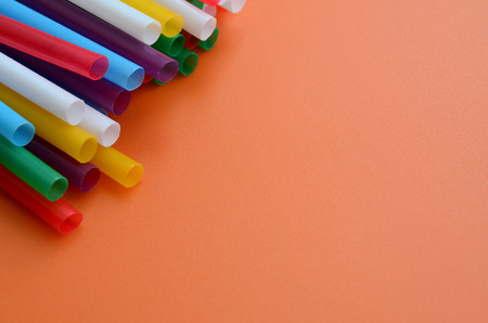 Many colorful straws for drinks lies on a bright orange background surfaceの写真素材