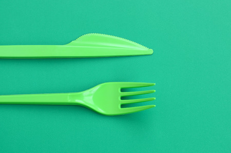 Disposable plastic cutlery green. Plastic fork and knife lie on a green background surface