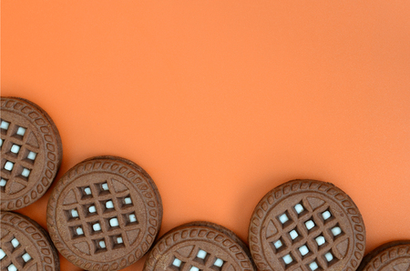 Detailed picture of dark brown round sandwich cookies with coconut filling on an orange surface....