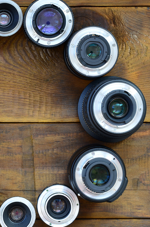Several photographic lenses lie on a brown wooden background. Space for textの写真素材