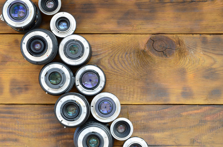 Several photographic lenses lie on a brown wooden background. Space for textの写真素材