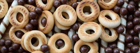 A lot of crispy sweet tubules, chocolate melting balls and yellow bagels lie on a wooden surface....