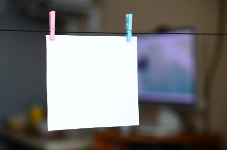 White blank card on rope, dark office background. Creative reminder, small sheet of paper on wooden clothespin, memo backdropの写真素材