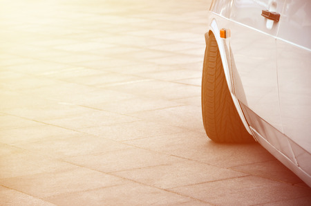 Diagonal view of a white glossy car that stands on a square of gray tiles