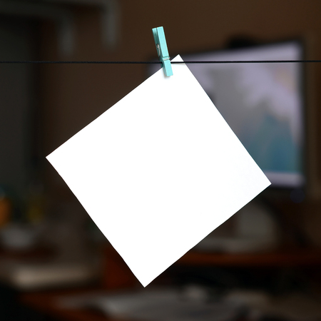 White blank card on rope, dark office background. Creative reminder, small sheet of paper on wooden clothespin, memo backdropの写真素材