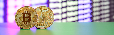 Two gold bitcoins lie on the green surface on the background of the display, which shows the process...